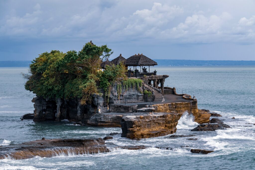 Tanah Lot temple located in Bali, Indonesia, features a sea temple on top of the cliff with waves crashing below.
