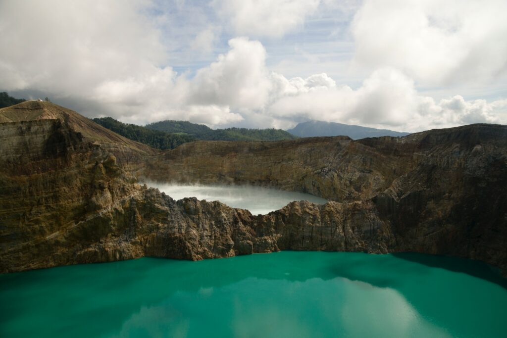The tri-color lakes of Kelimutu reflect clouds and the blue sky.