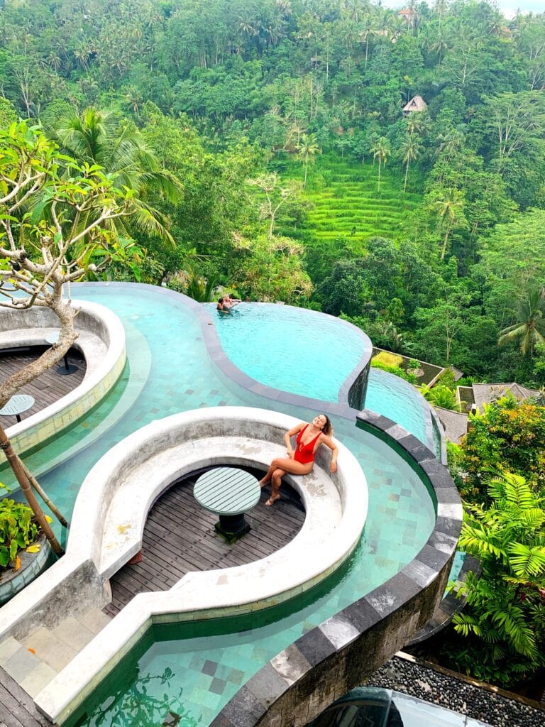 A girl in a red bathing suit sits on a chair next top an infinity pool in bali.
